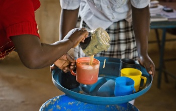 A volunteer from Zambia serving Mary's Meals to children at school. 
