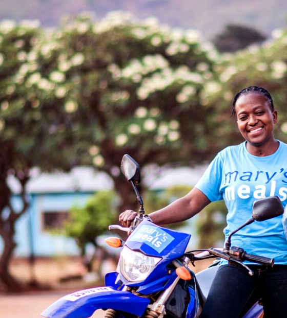 A volunteer in Zambia rests against her motorbike