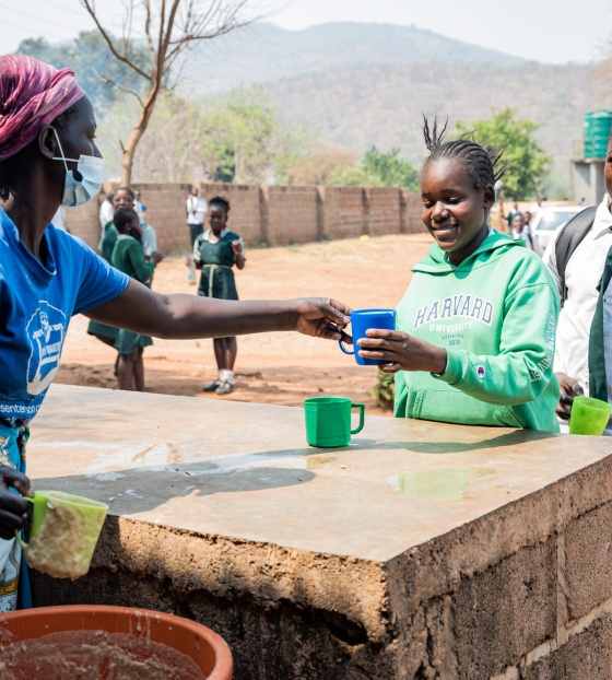 a queue of people collecting food from a woman serving behind a table 