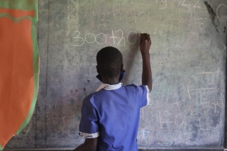 A child from Zambia writing on the chalk board in class.