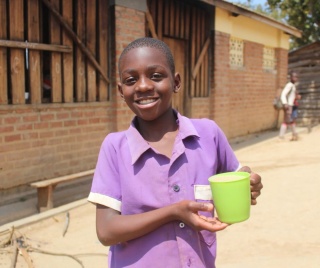 Shark, a school pupil from Malawi smiles and he holds his nutritious mug of porridge.