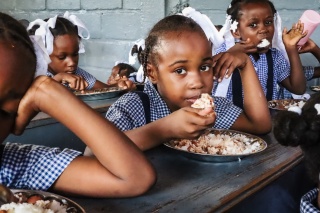 A school girl in Haiti eating from a plate of food. 